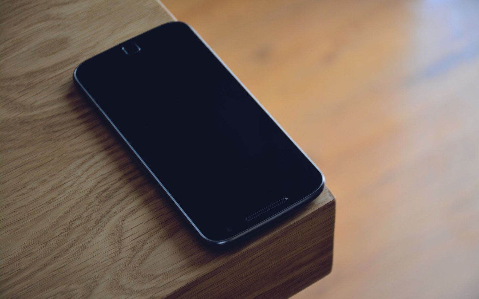 A black smartphone with a dark screen resting on the edge of a wooden table