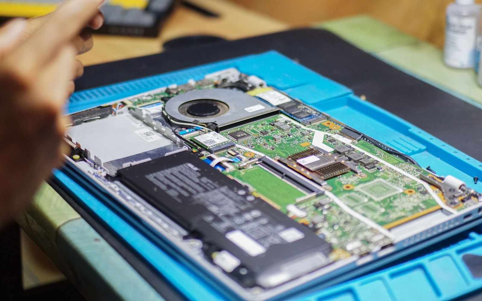 A technician points at the exposed motherboard and cooling fan of a disassembled laptop