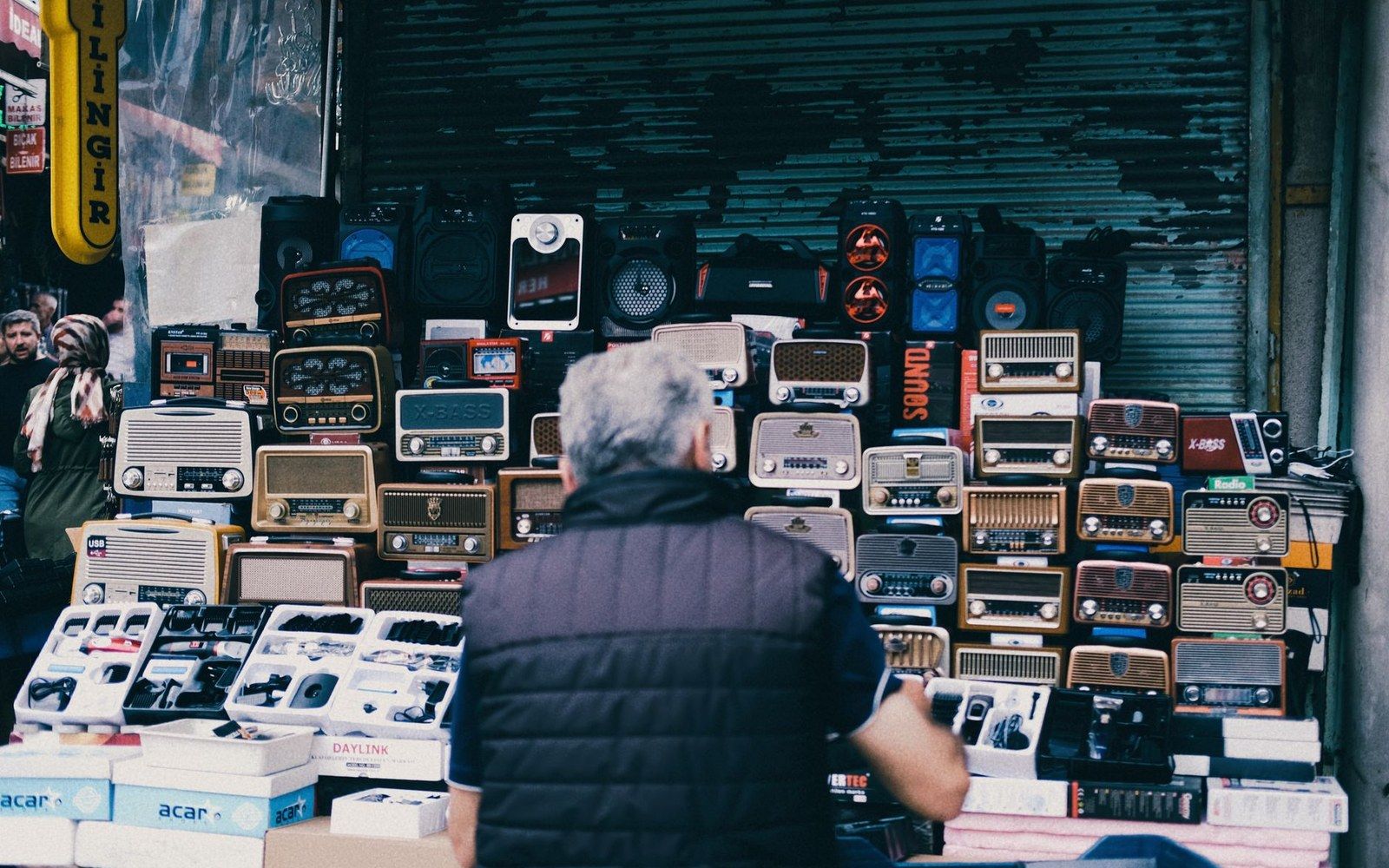 A man stands before a market stall stacked with vintage-style radios and speakers