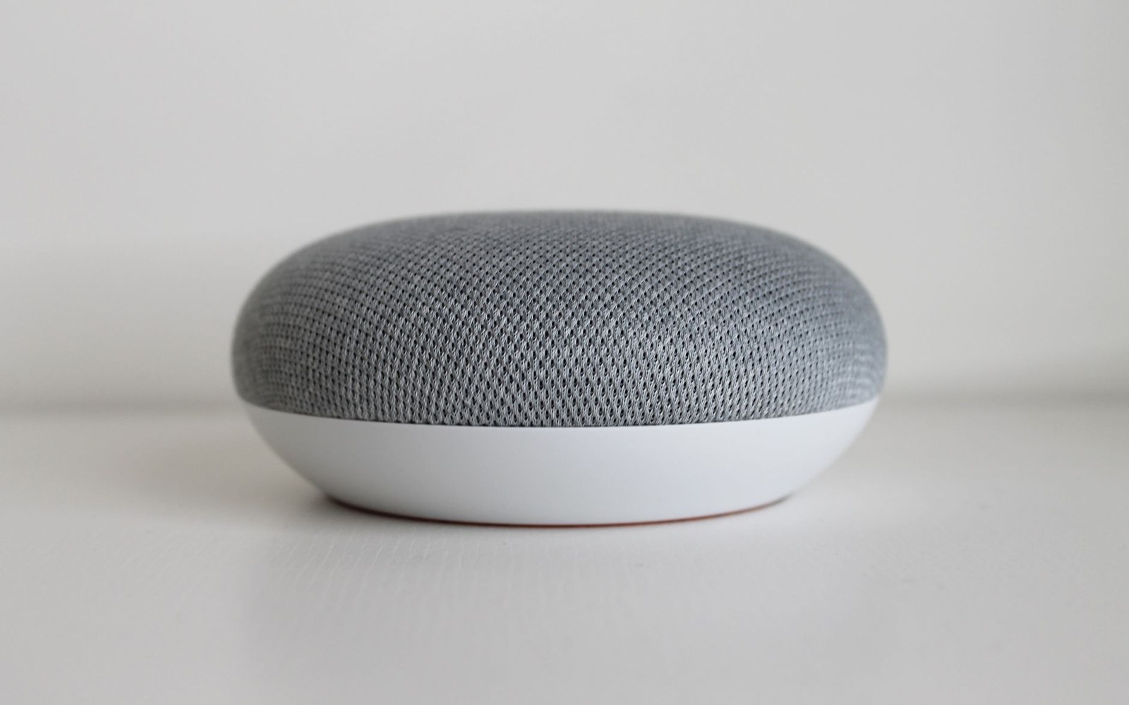Small round smart speaker with gray fabric top and white base on a table