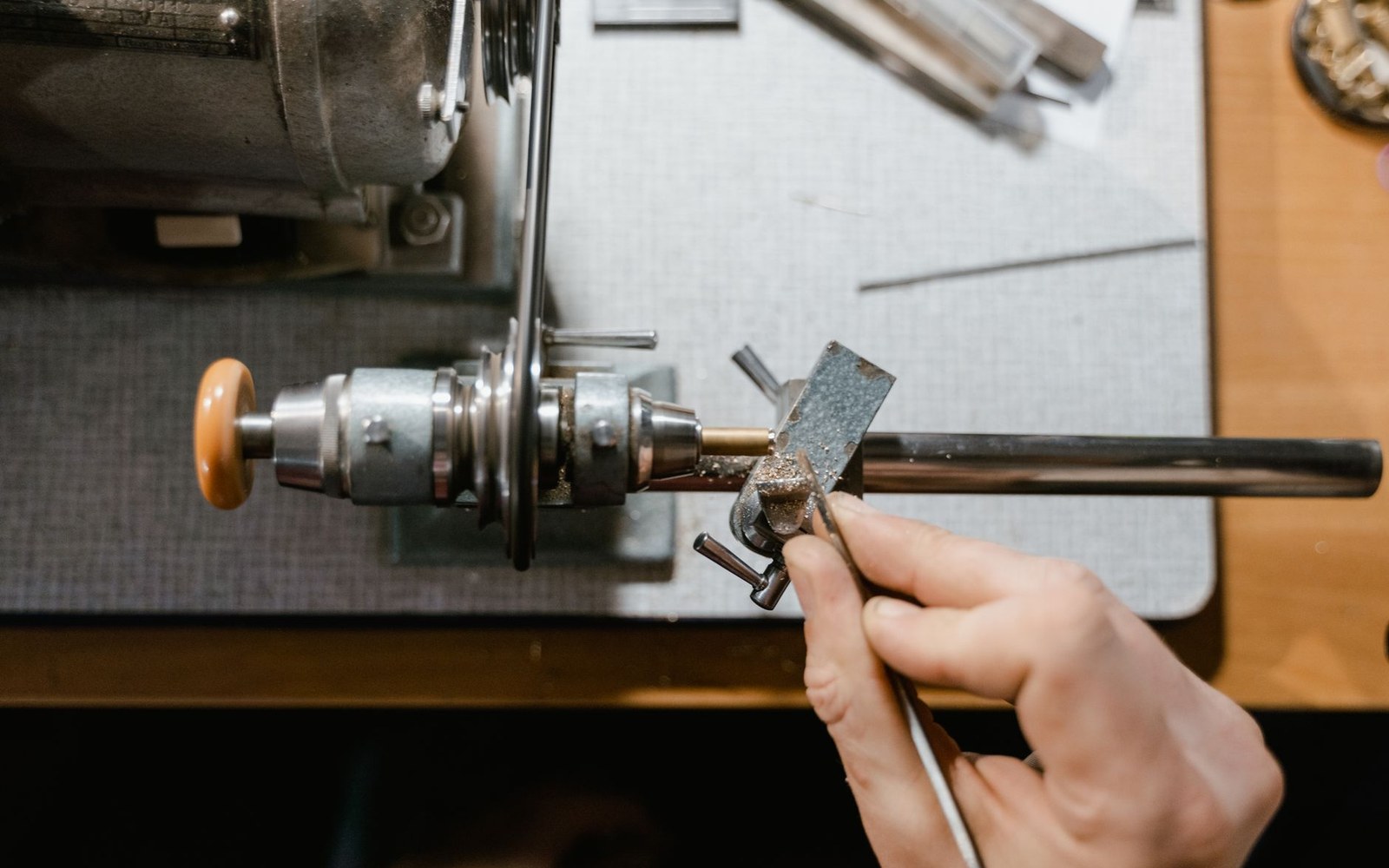 A hand holds a metal rod against a bench polishing wheel for shaping