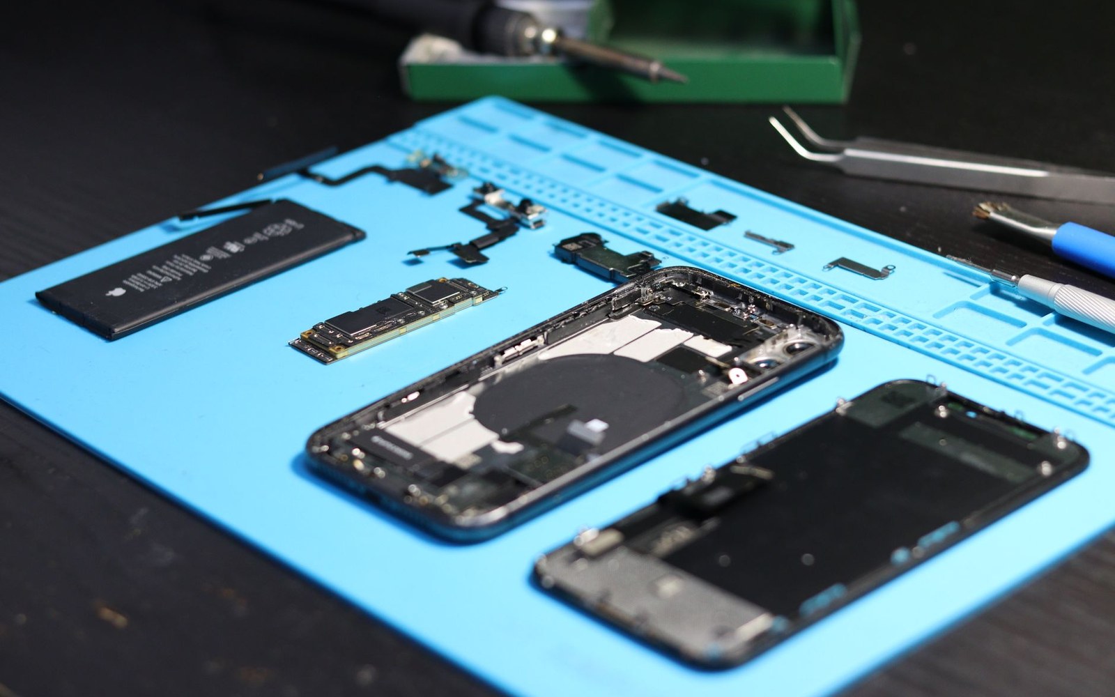 A disassembled smartphone with battery and circuit boards laid out on a repair mat